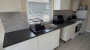 Una cocina moderna con encimera negra, armarios blancos, horno integrado y una ventana con persianas.
