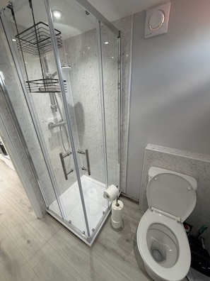 Un baño moderno con ducha acristalada, inodoro y suelo de mármol.