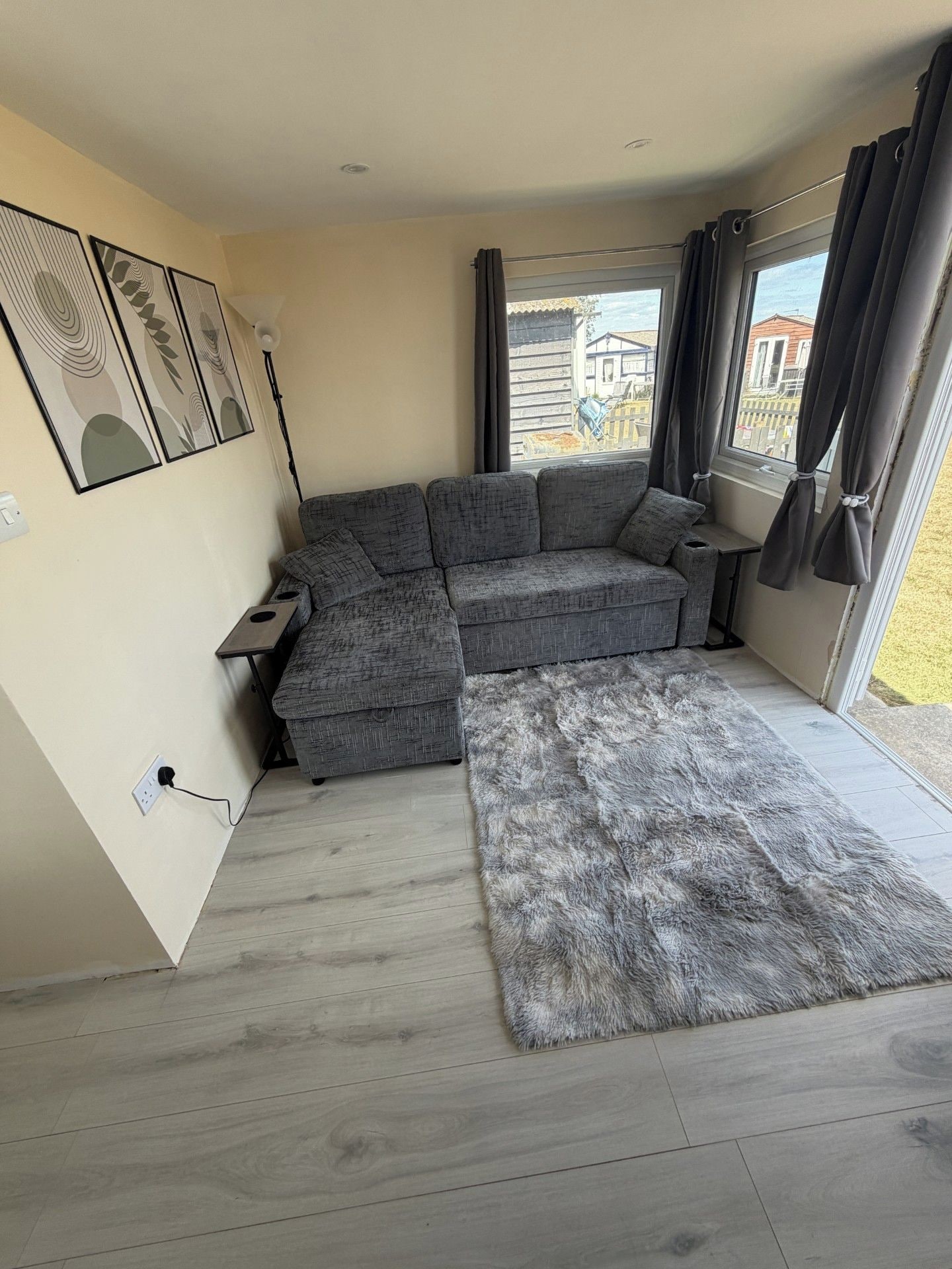 Un salon moderne avec un canapé d’angle gris, un tapis gris moelleux et une grande fenêtre avec des rideaux.