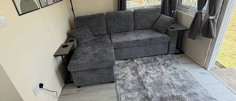 Un salon moderne avec un canapé d’angle gris, un tapis gris moelleux et une grande fenêtre avec des rideaux.