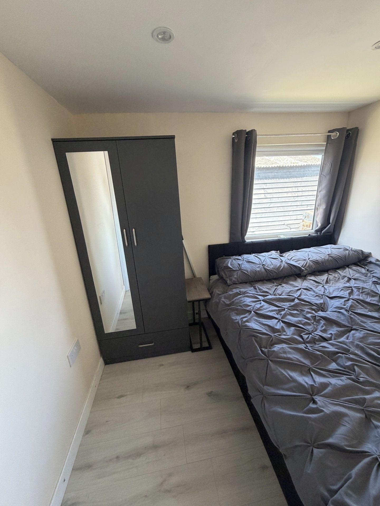 A bedroom with a bed, a wardrobe, a window with curtains, and a ceiling light.