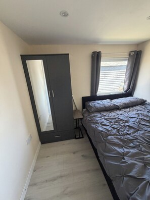 Un dormitorio con cama, armario, ventana con cortinas y una lámpara de techo.
