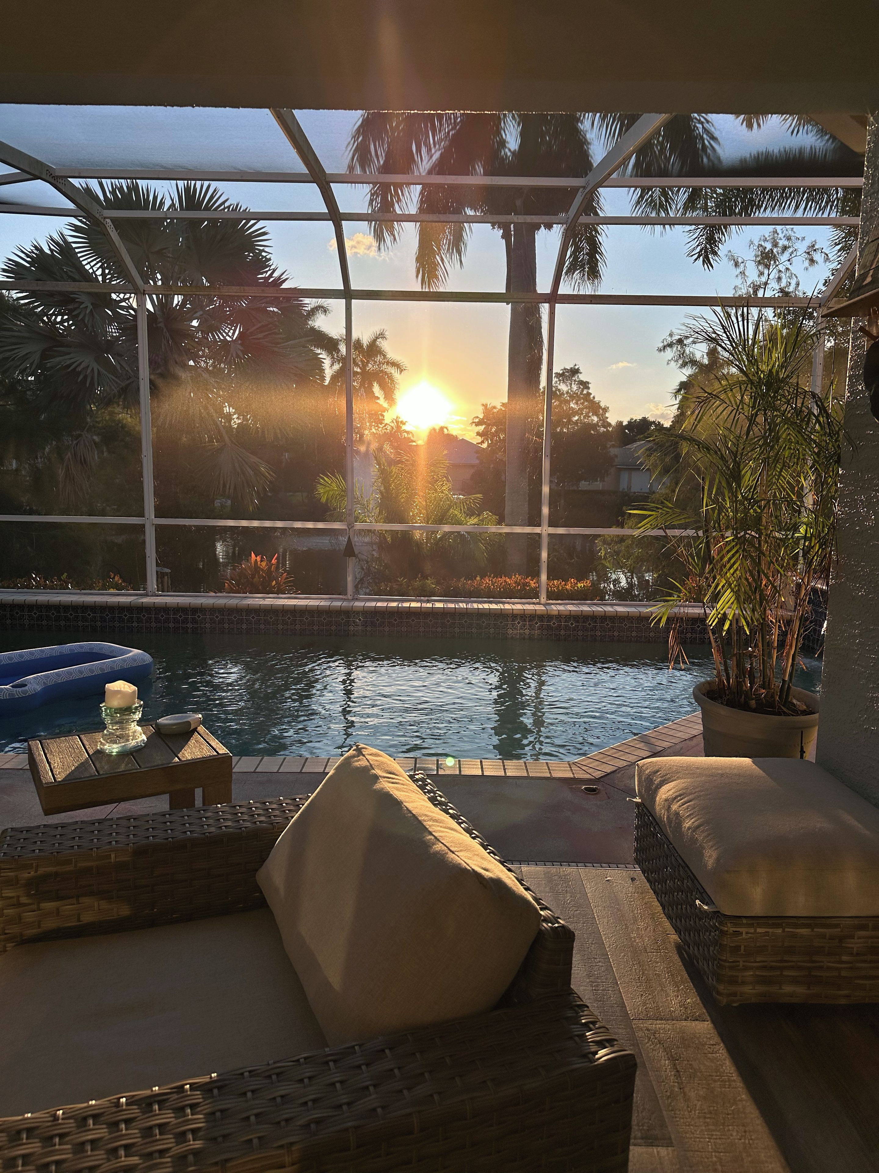Un área junto a la piscina con vista al atardecer, una silla de descanso, una mesita con una vela y una planta en maceta.