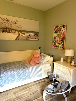 Een slaapkamer met een eenpersoonsbed, een babybedje, een wandlamp en twee schilderijen.