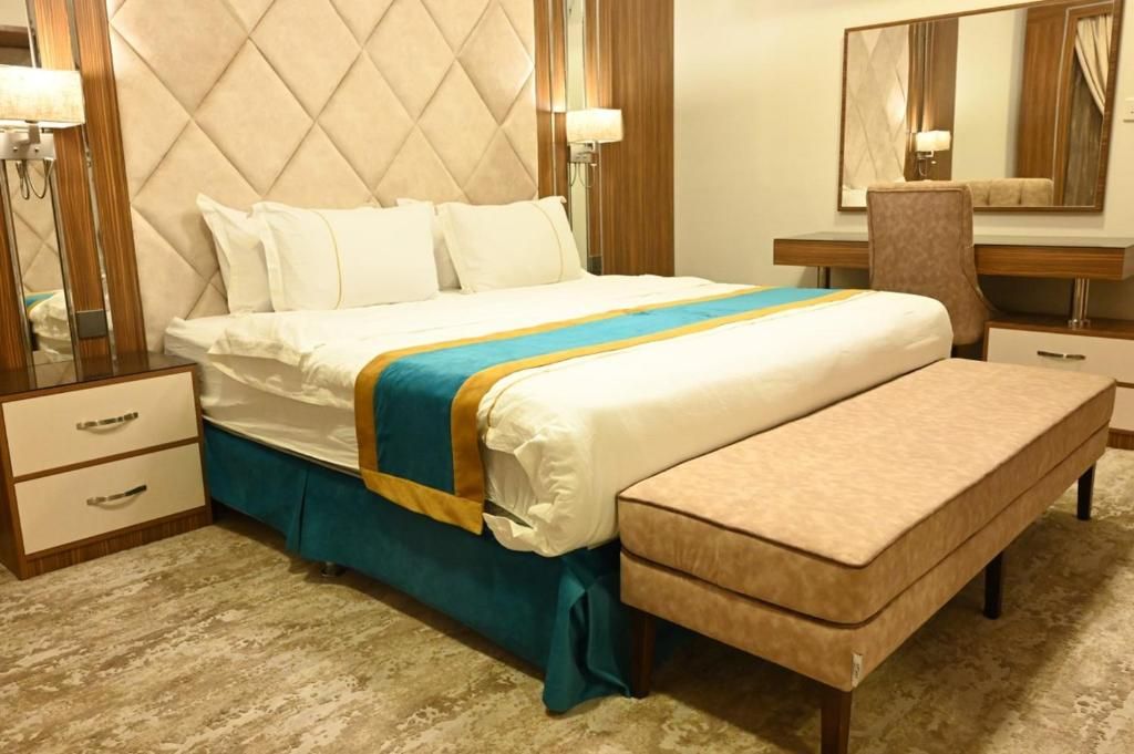 Habitación de hotel con una cama grande, una mesita de noche, una silla, un escritorio y un espejo.