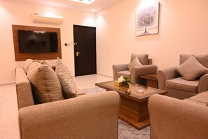 A living room with sofas, a coffee table, a flat-screen TV, and a door. - Jawharat Al Sarat for hotel apartments (Al-Amjad District)