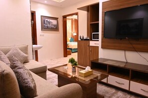 Ein modernes Wohnzimmer mit Sofa, Couchtisch, Fernseher und einer Küchenzeile im Hintergrund.