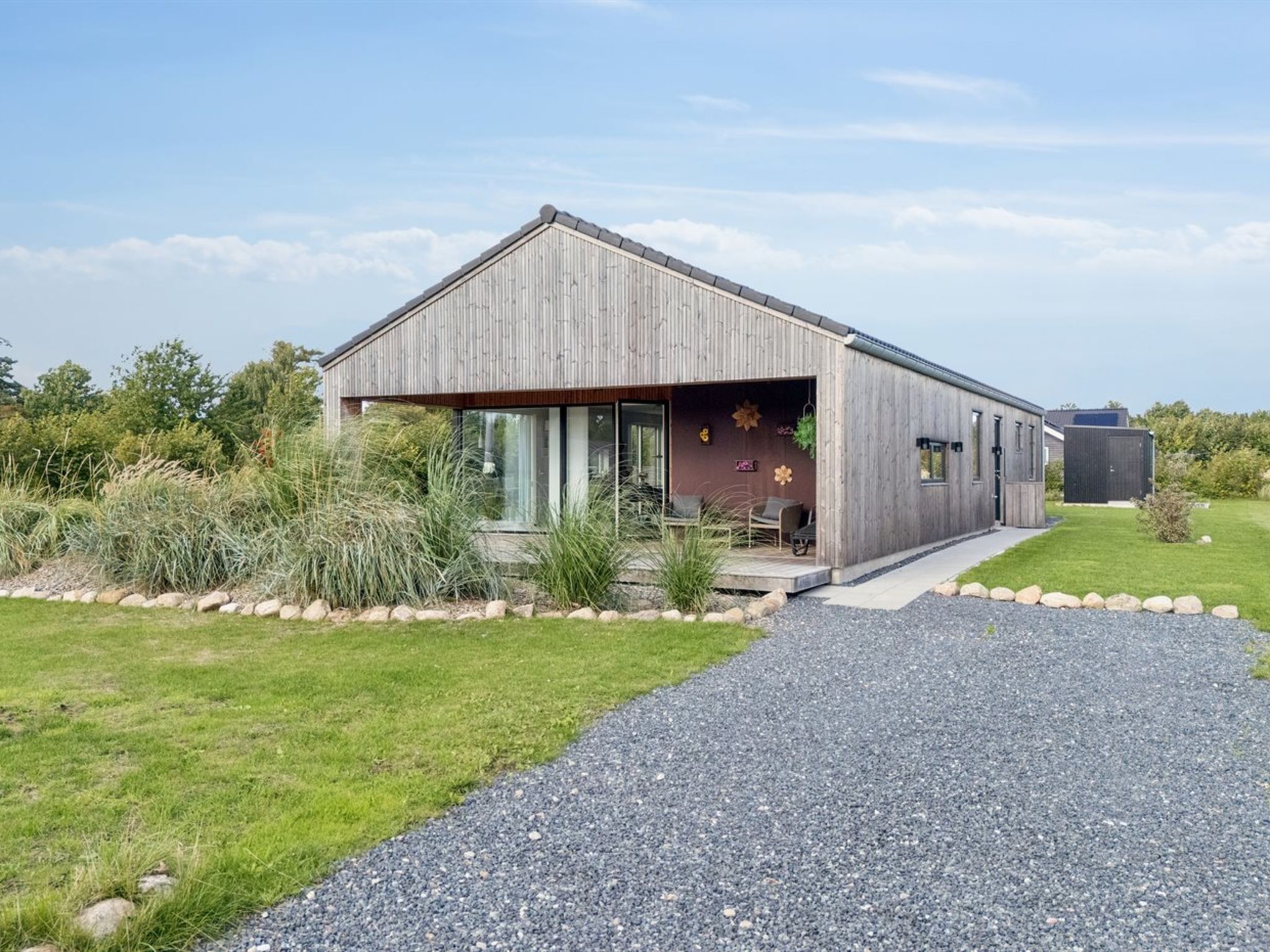 A modern wooden house with a large garage, surrounded by a well-maintained lawn and gravel driveway.