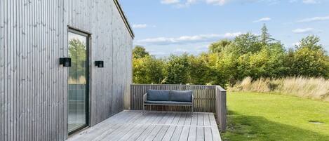 Une terrasse extérieure moderne, dotée d’un banc intégré, d’une porte-fenêtre et d’une clôture en bois.