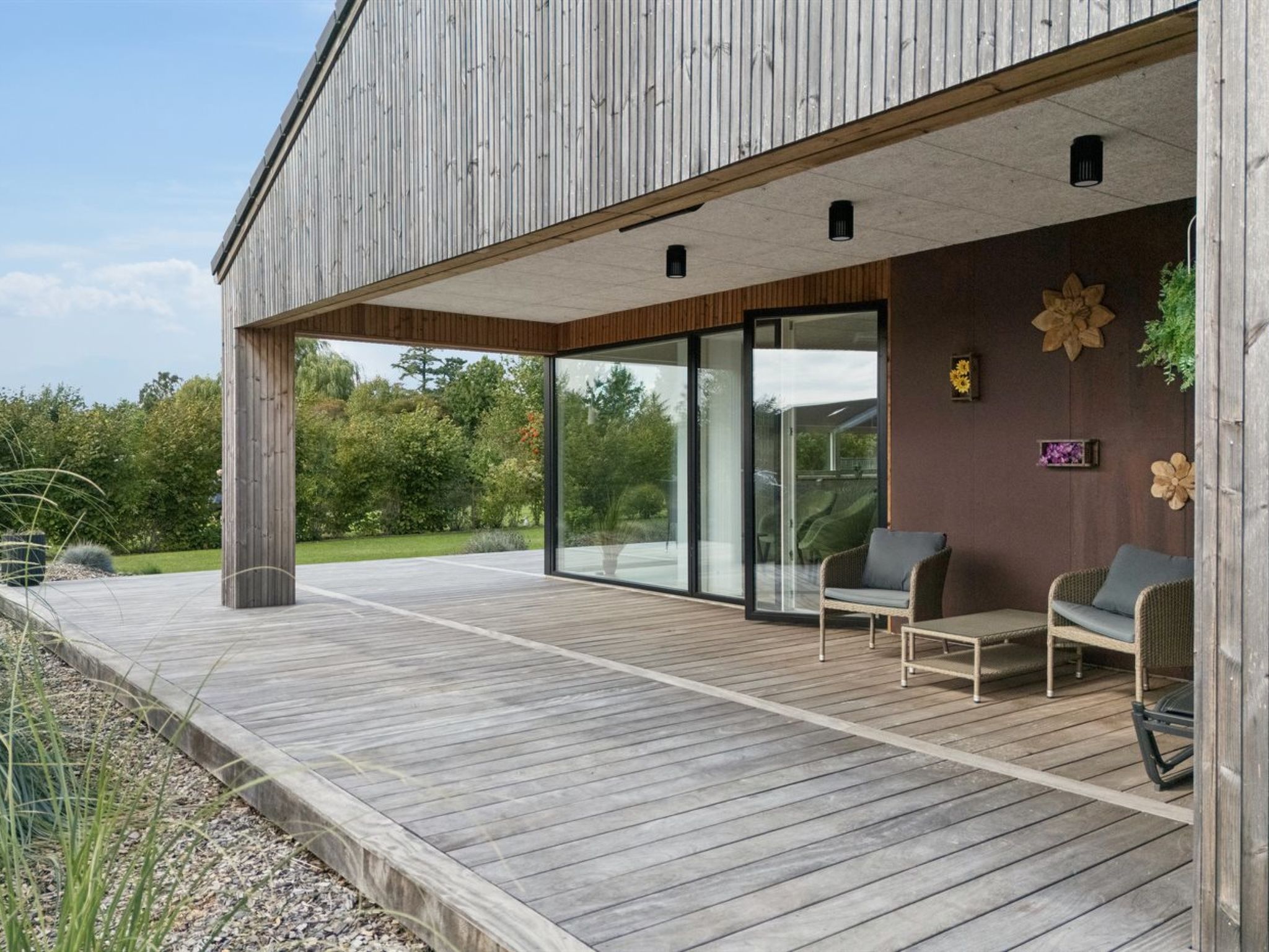 Un edificio moderno con terraza de madera, puertas correderas de vidrio y mobiliario exterior.