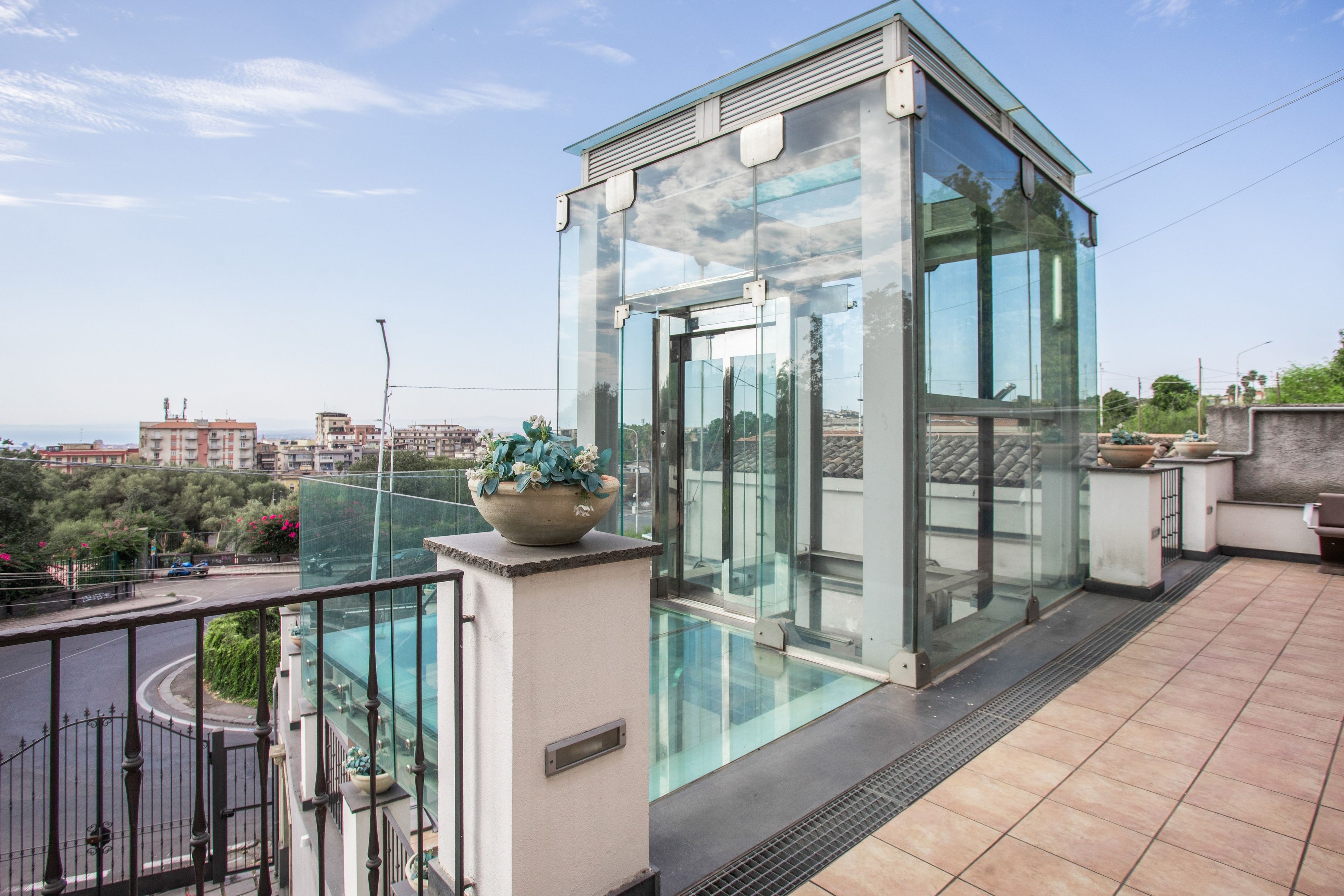 A modern glass elevator on a rooftop terrace with a clear view of the cityscape.