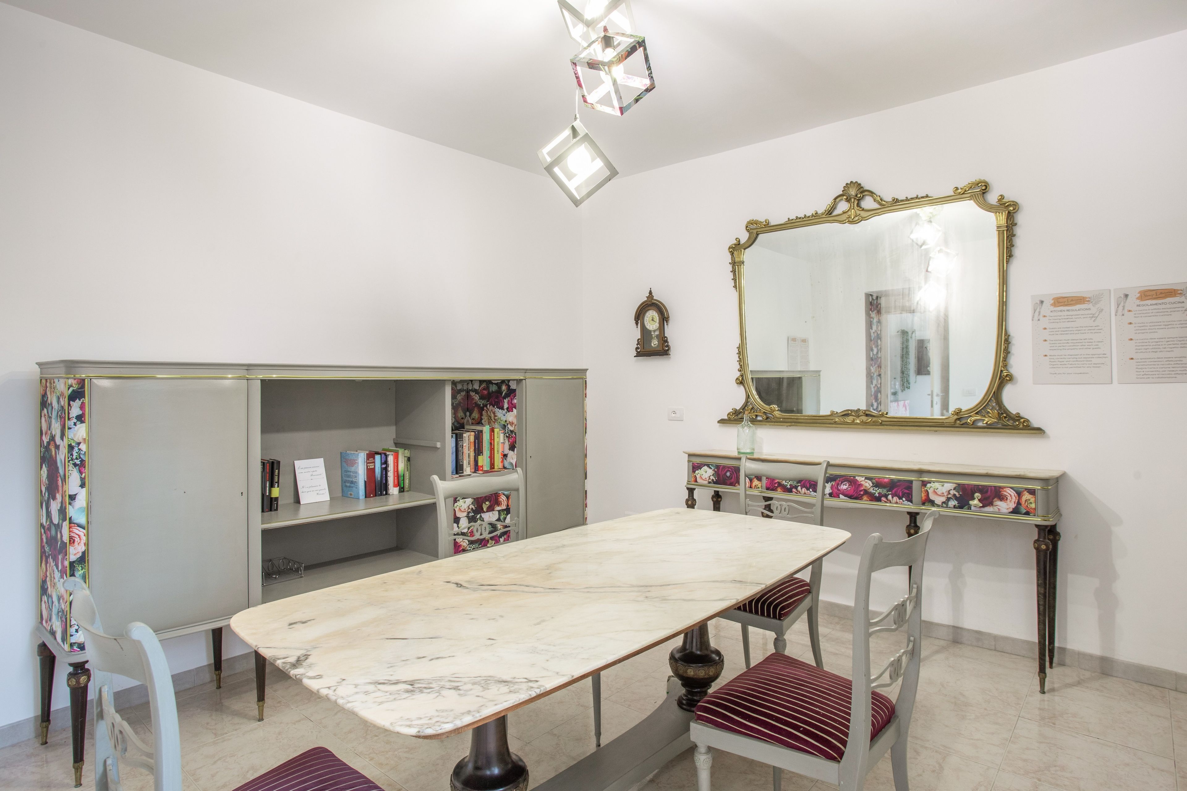 Zona pranzo con tavolo in marmo, sedie, una libreria, uno specchio e un orologio appeso al muro.