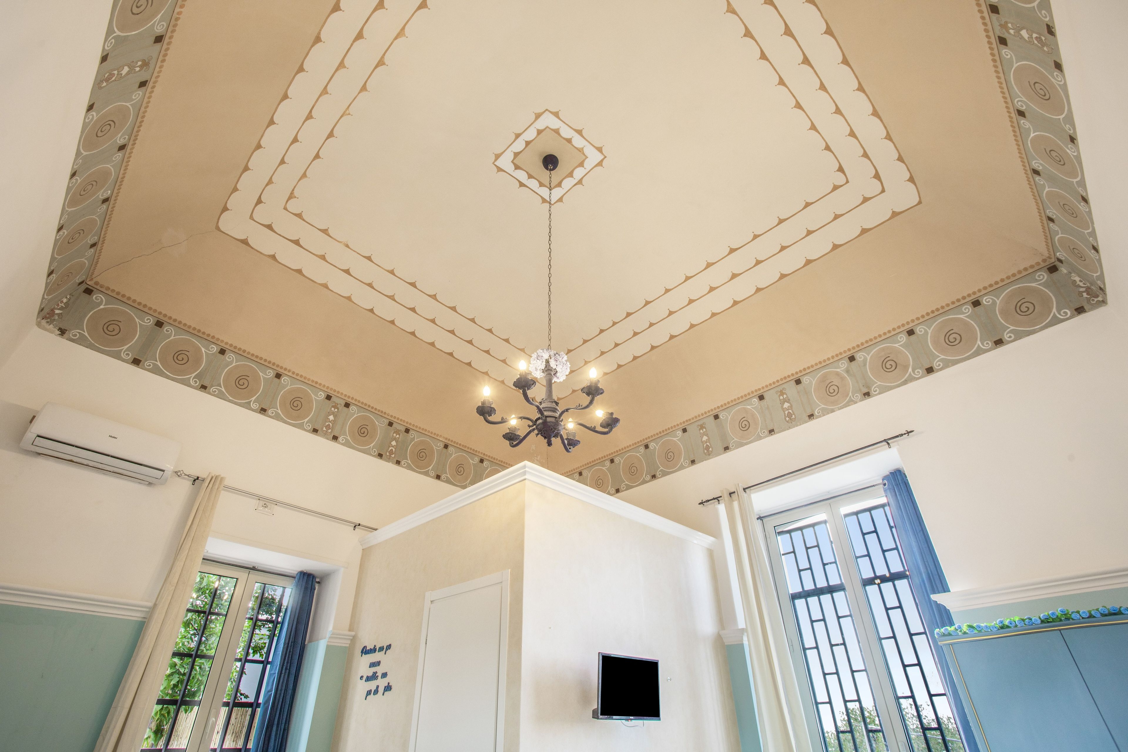 A room with a decorative ceiling, a chandelier, an air conditioning unit, and a window with bars.