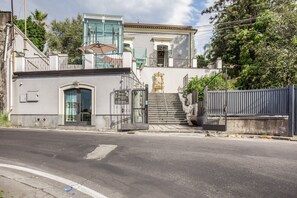 A building with a gated entrance, a staircase leading to a balcony, and a clear sky. - Stanze Letterarie - 'Giovanni Verga' (Catania)