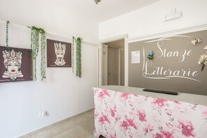 A reception area with a floral-patterned desk, framed artwork on the wall, and a sign that reads 'Stanze Letterarie'. - Stanze Letterarie - 'Giovanni Verga' (Catania)