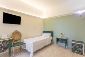 A hotel room with a bed, a chair, a small table with a vase, and a television mounted on the wall. - Stanze Letterarie -  'Mario Grasso'  (Catania)