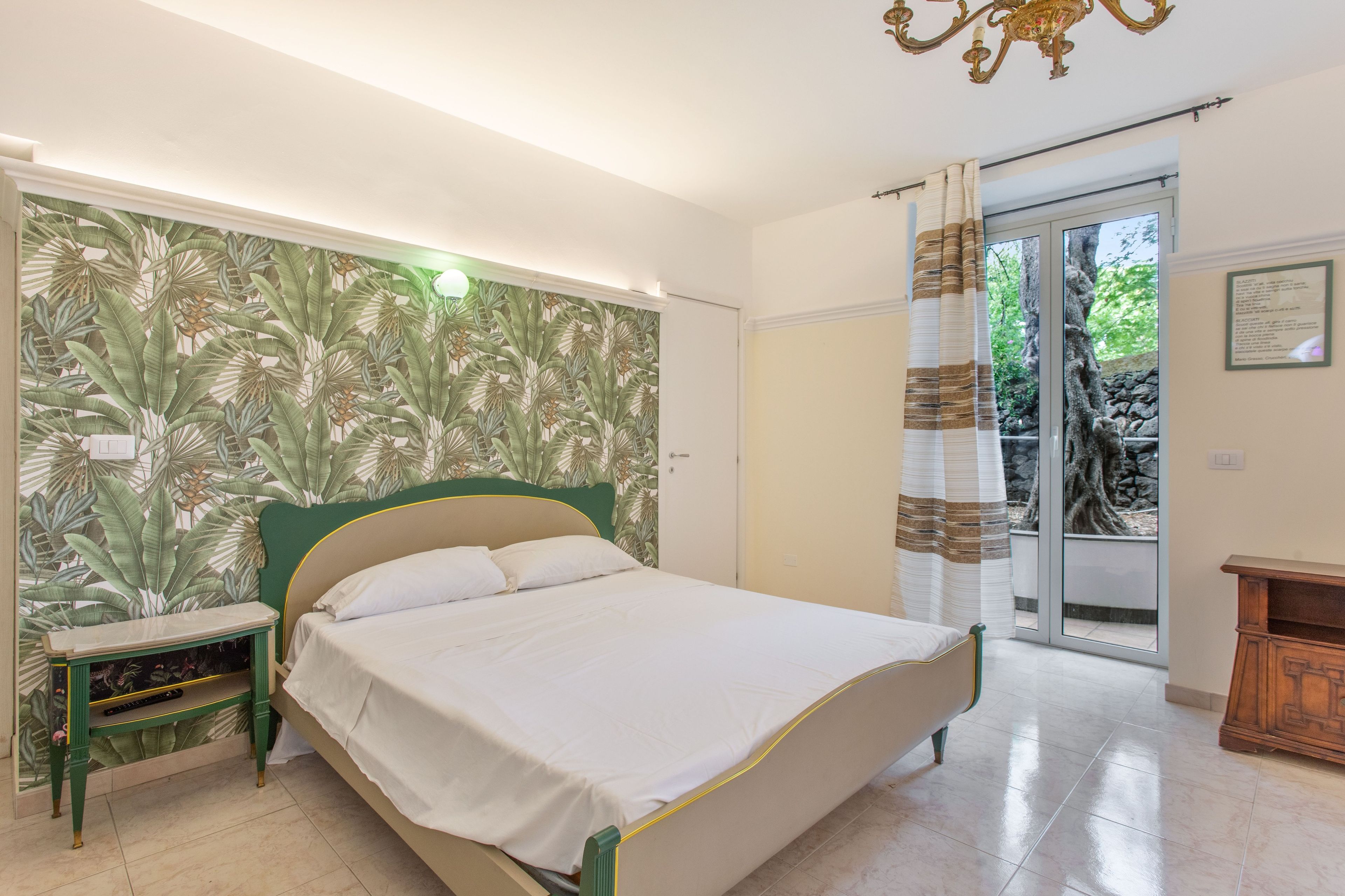 A bedroom with a bed, a nightstand, a mirror, a chandelier, and a view of the outdoors through a sliding door.