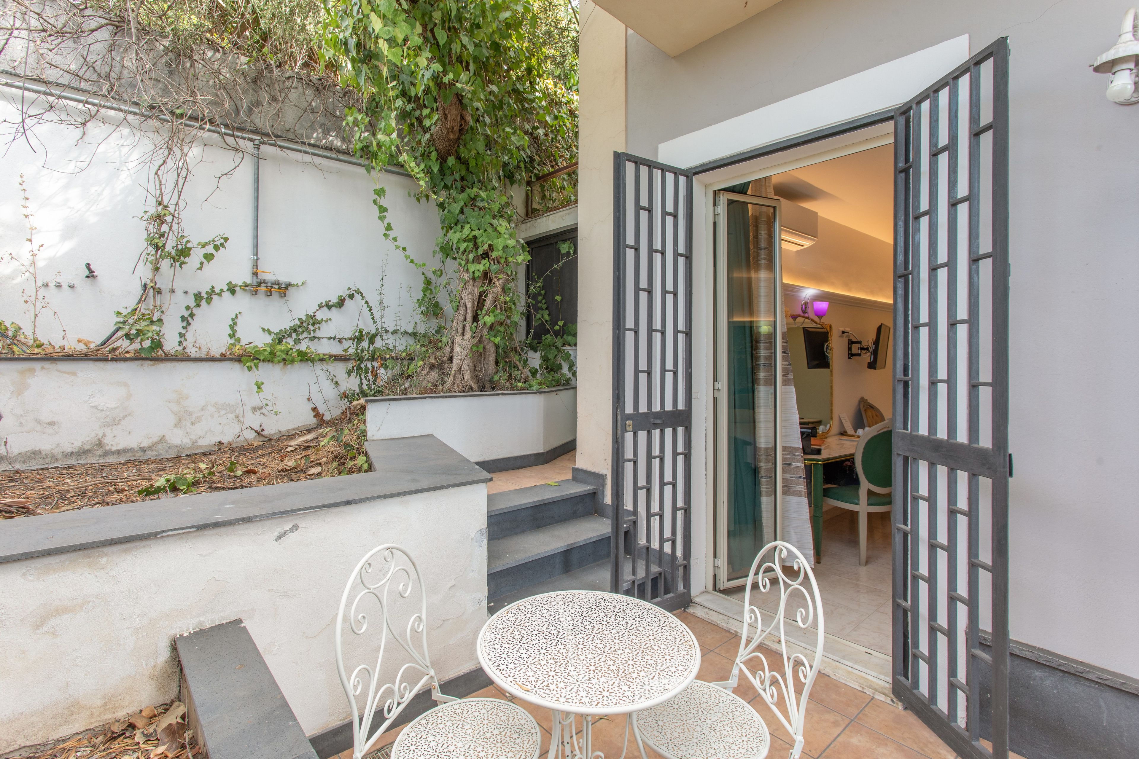An outdoor seating area with a table and chairs, a staircase leading to a door, and a wall with climbing plants.