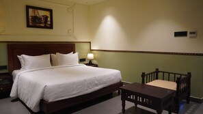 Ein Hotelzimmer mit einem großen Bett, einem Nachttisch, einer Nachttischlampe, einem Holzsessel und einem Bild an der Wand.