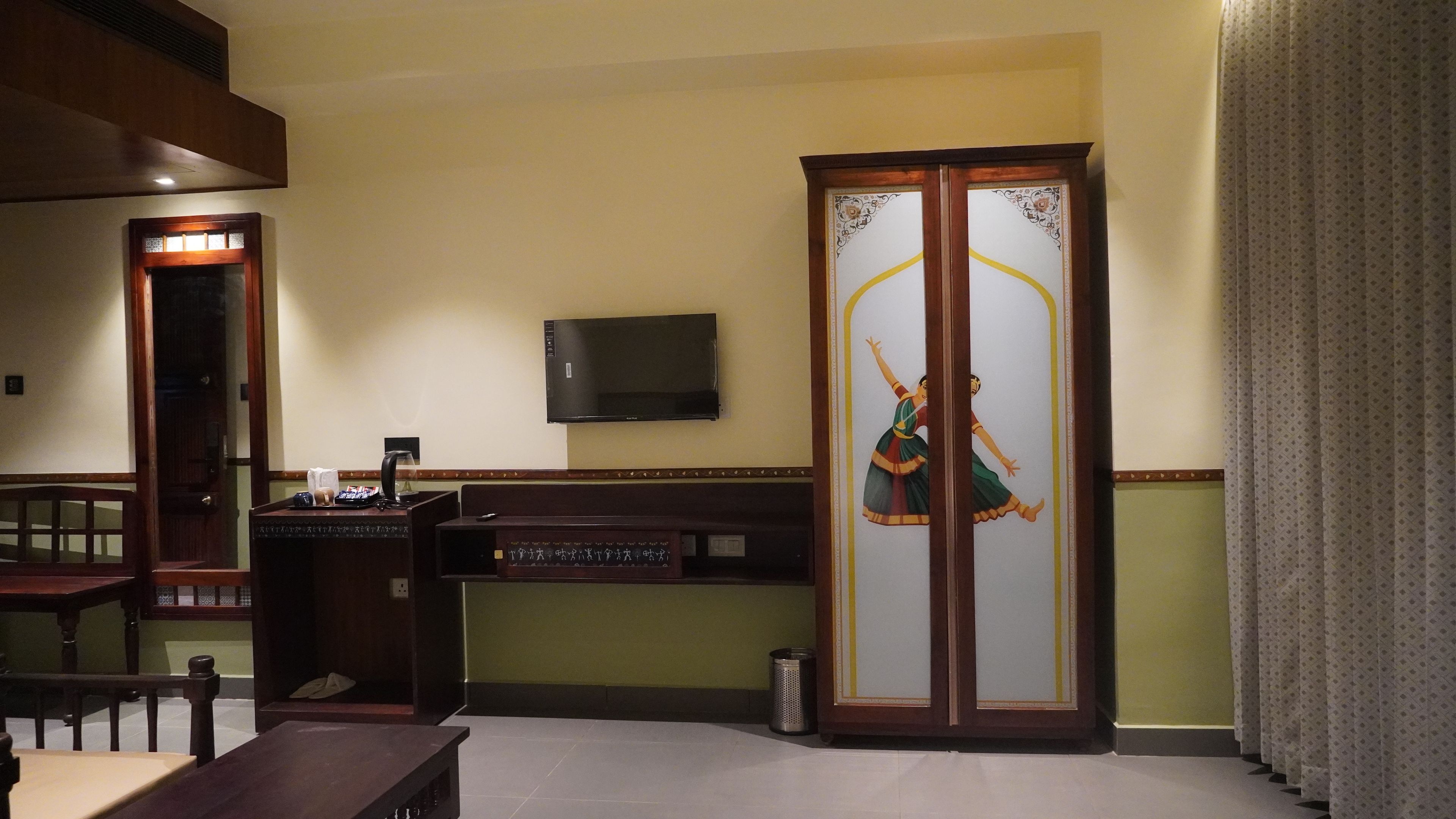 Una habitación con un escritorio de madera, un televisor montado en la pared y un mueble decorativo con puerta de vidrio.