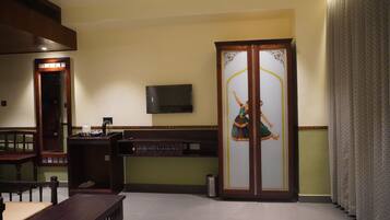 Una habitación con un escritorio de madera, un televisor montado en la pared y un mueble decorativo con puerta de vidrio.