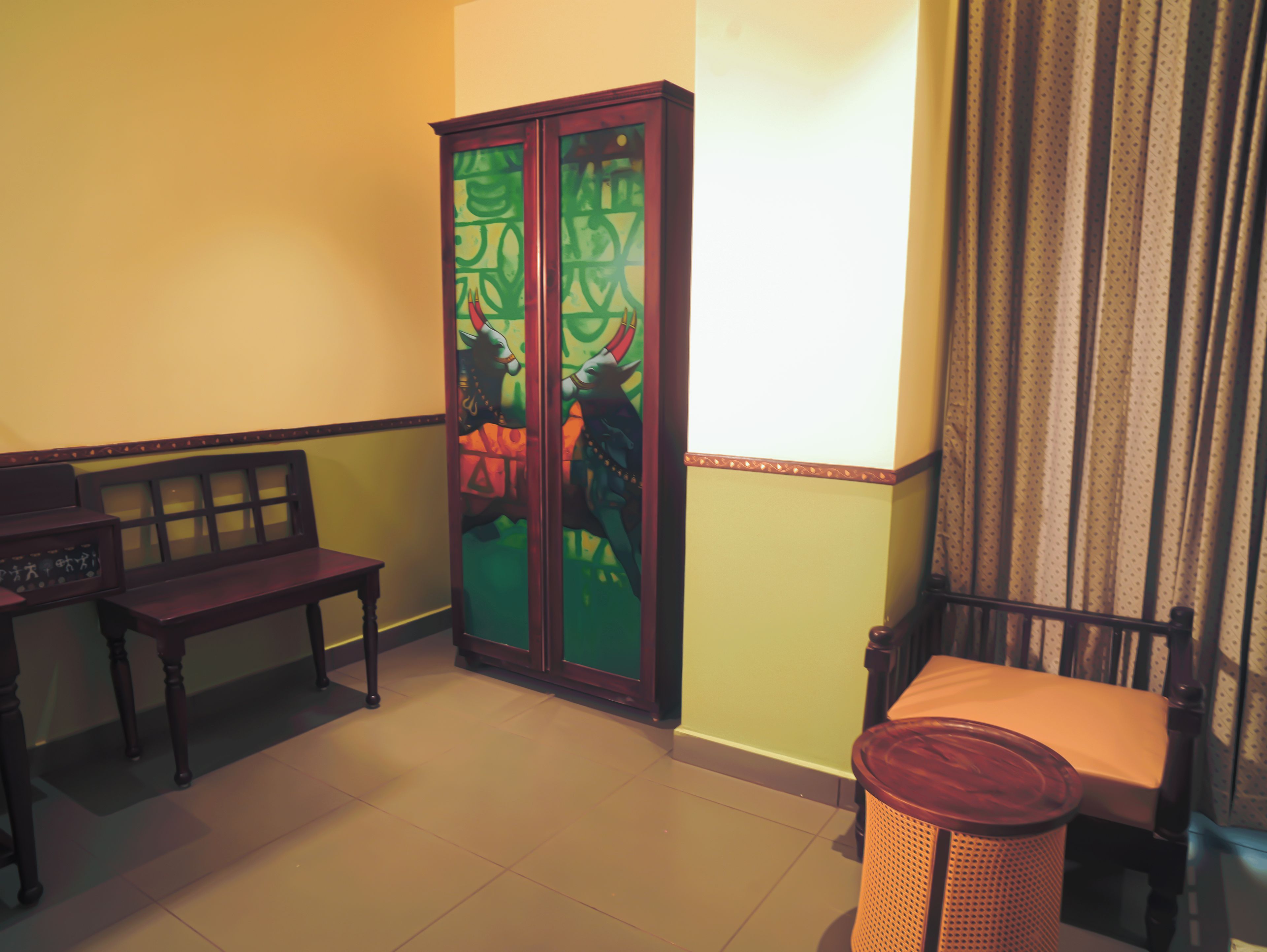 Una habitación con un armario de madera, un banco, una silla y un cubo de basura.