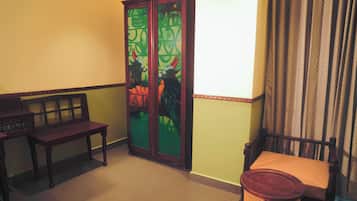 Una habitación con un armario de madera, un banco, una silla y un cubo de basura.