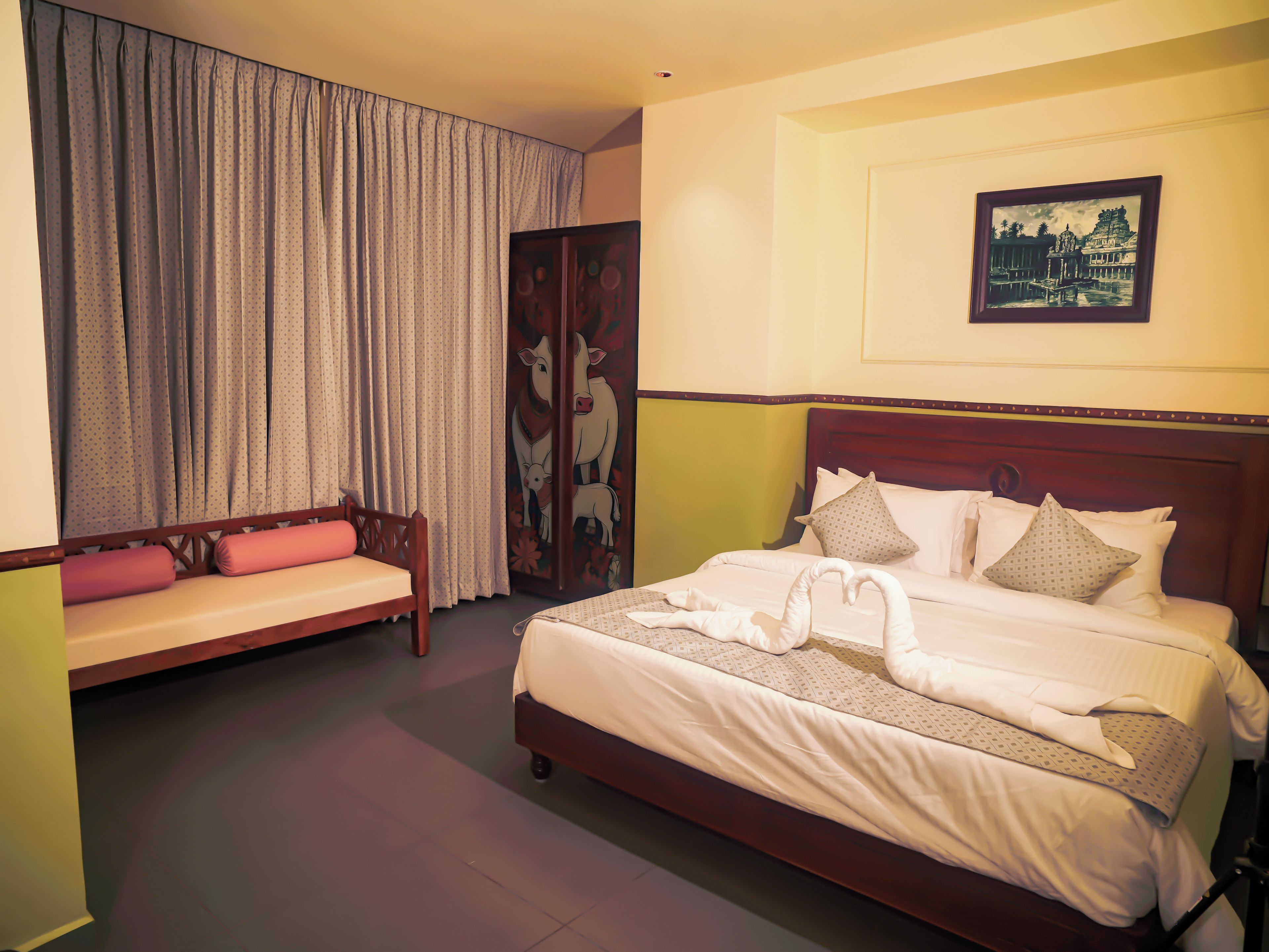 A hotel room with a bed, a sofa, a large window with curtains, and a wall-mounted picture.