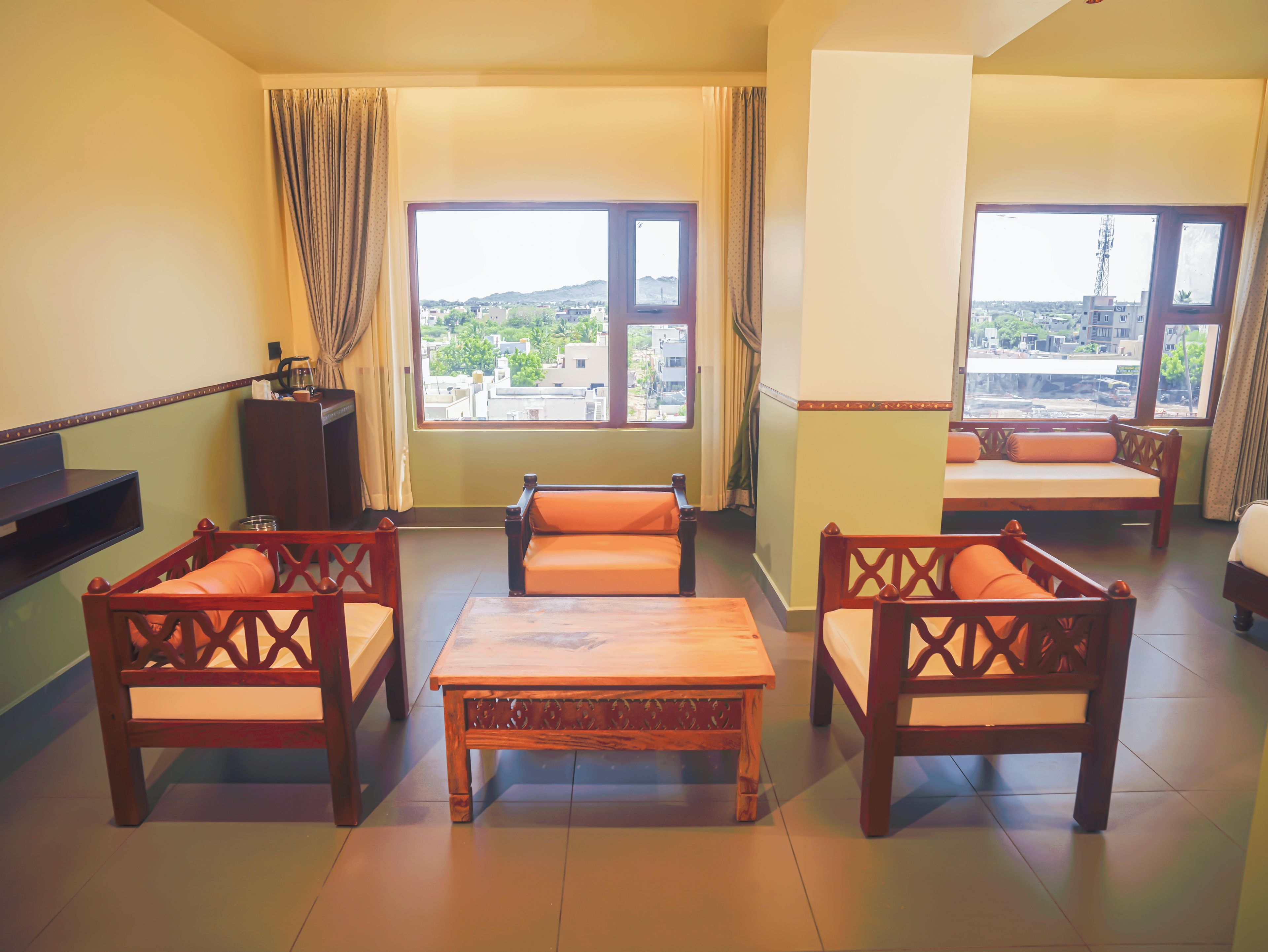 A room with a sofa set, a wooden table, and a view of a cityscape through large windows.