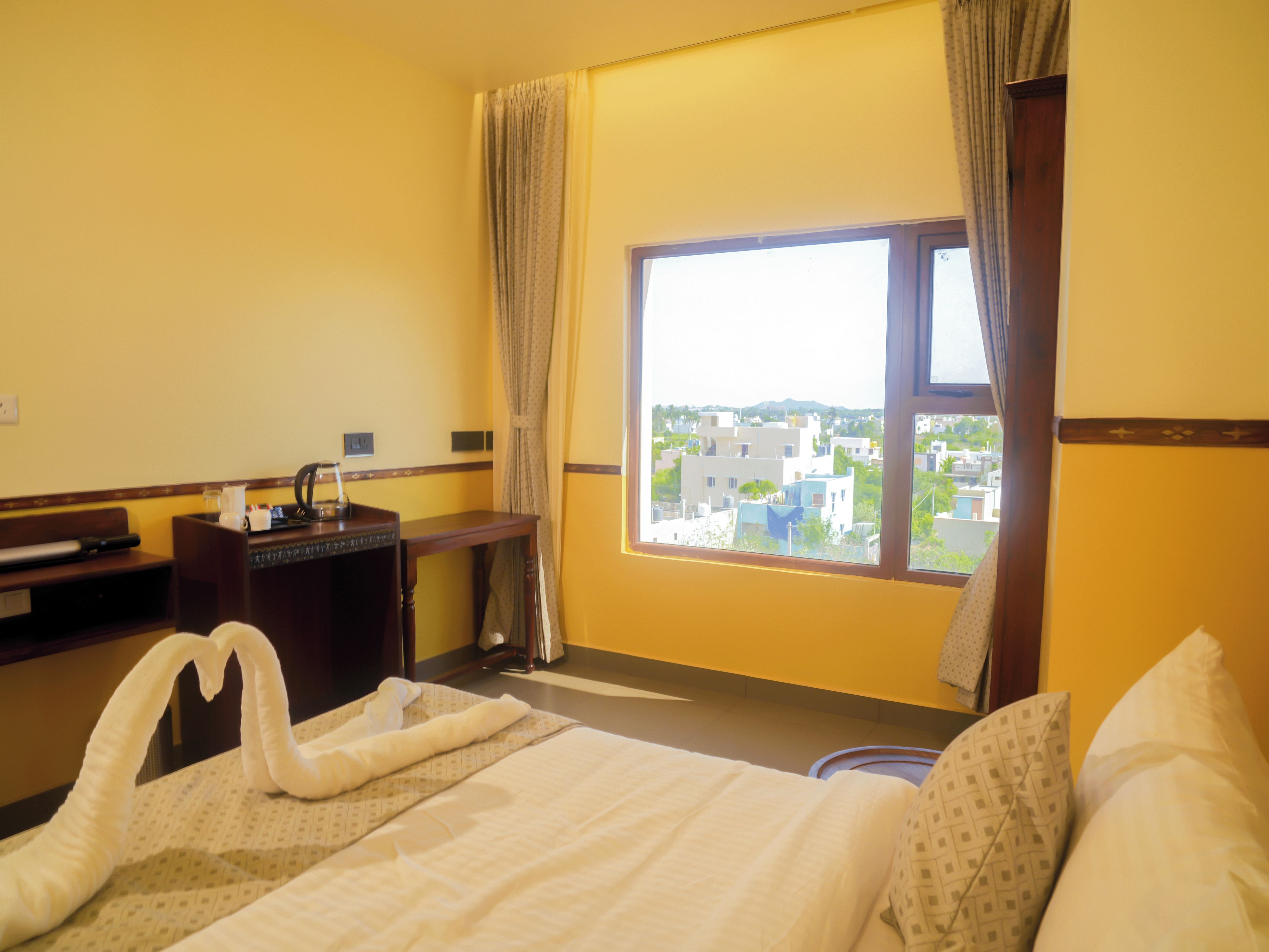 Habitación de hotel con cama, escritorio, ventana con vista a la ciudad y un par de toallas sobre la cama.