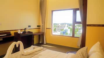 Habitación de hotel con cama, escritorio, ventana con vista a la ciudad y un par de toallas sobre la cama.