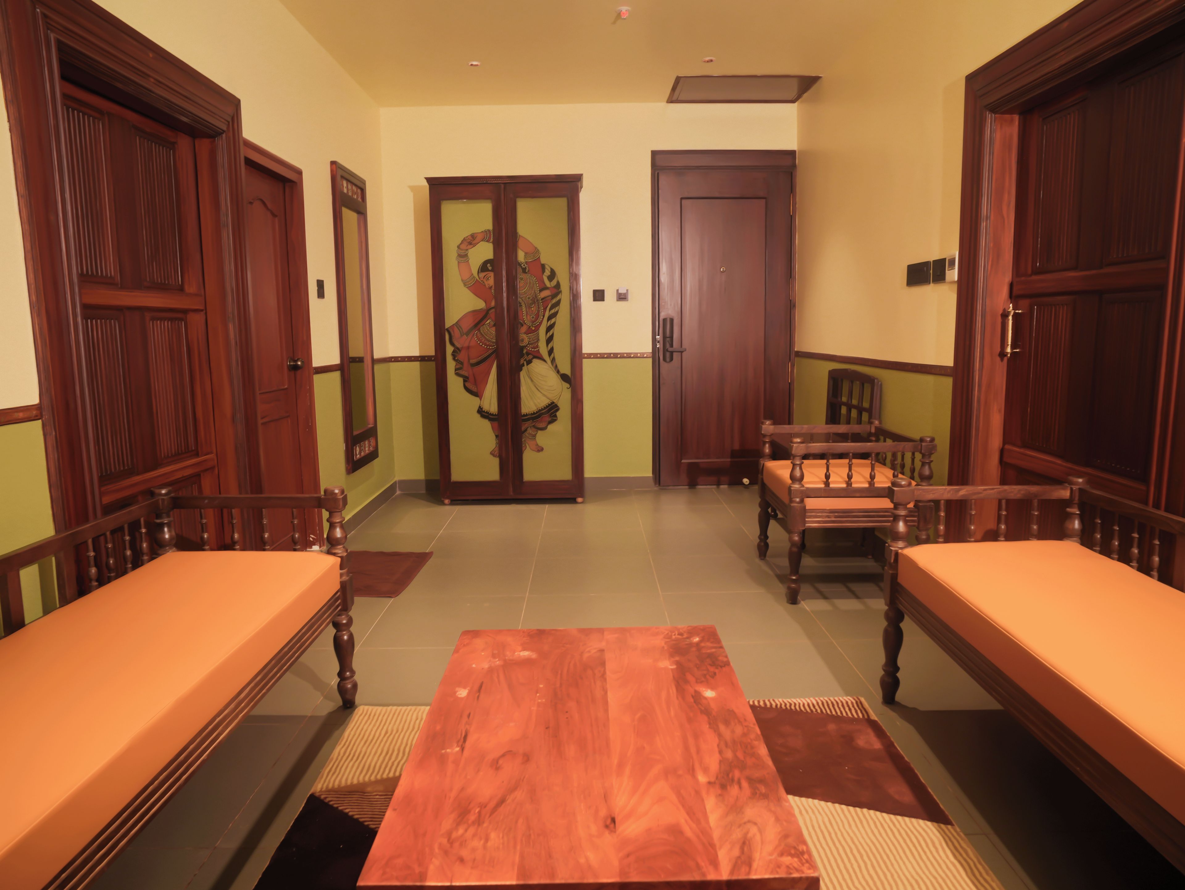 Una habitación con una mesa de madera, dos bancos de madera, una puerta con un espejo y una pared con un panel decorativo.