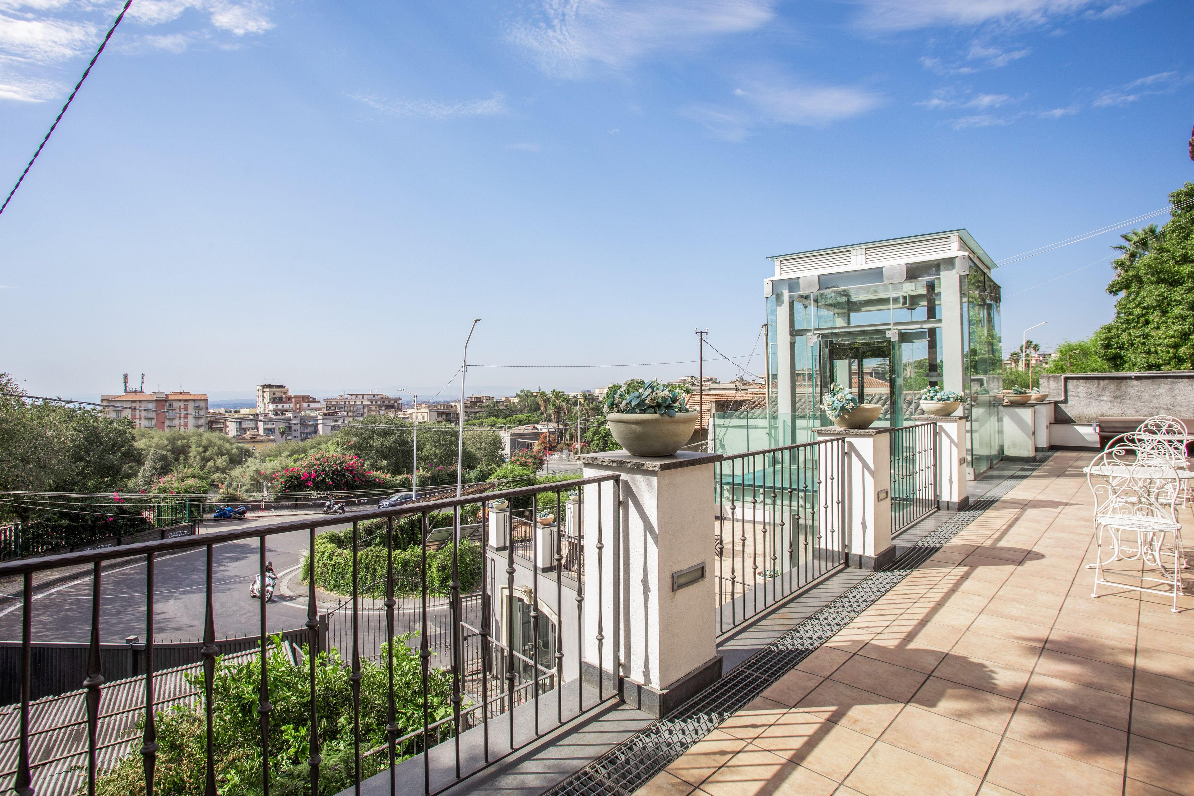 A rooftop terrace with a glass elevator, potted plants, and a view of the cityscape.