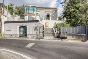 A building with a gated entrance, a staircase leading to a balcony, and a clear sky. - Stanze Letterarie – 'Rosa Balistreri' (Catania)