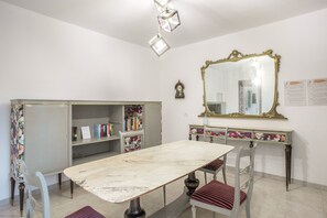 A dining area with a marble table, chairs, a bookshelf, a mirror, and a clock on the wall. - Stanze Letterarie – 'Rosa Balistreri' (Catania)
