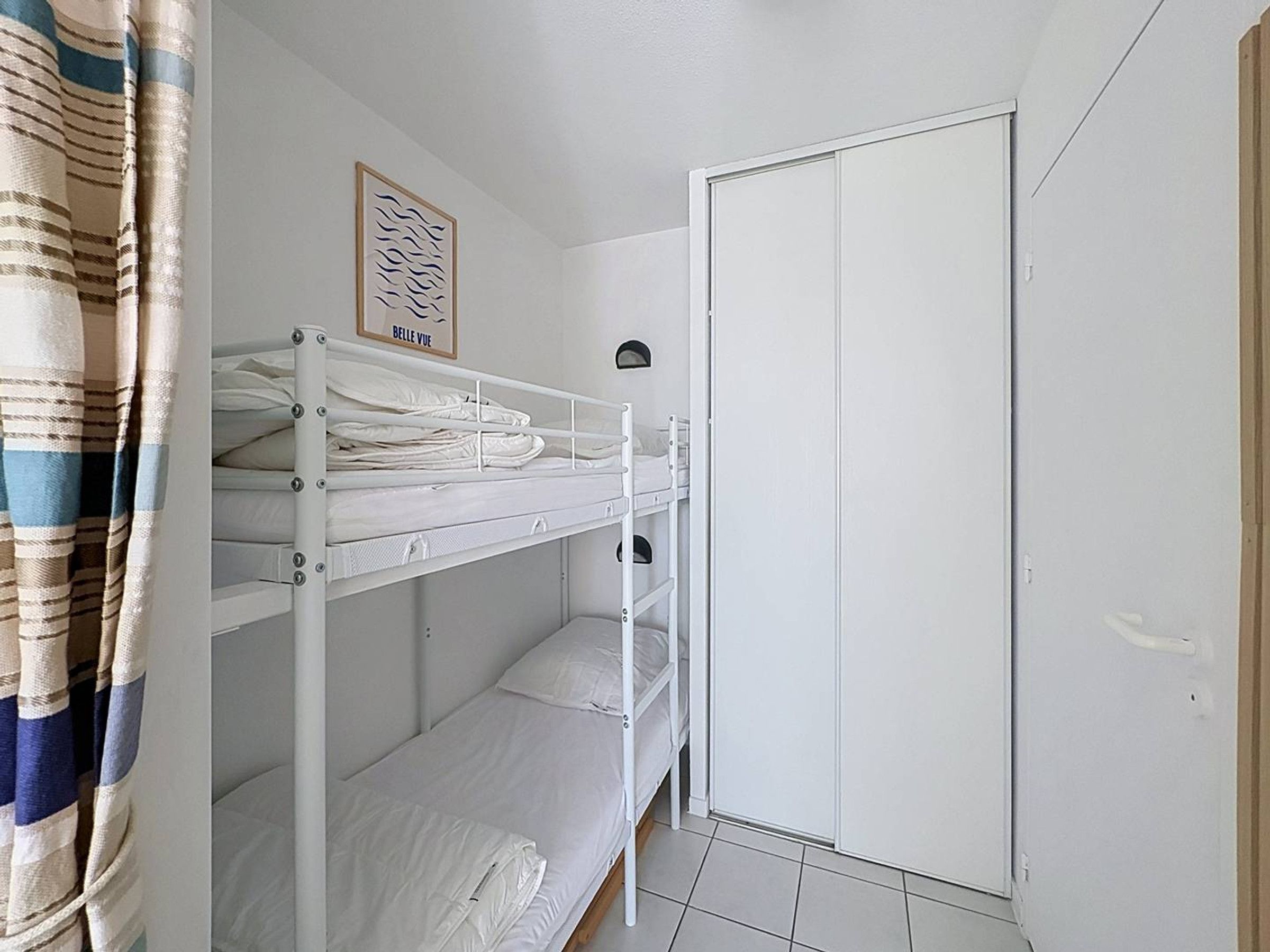 Een slaapkamer met stapelbed, een witte garderobe en een foto in een lijst aan de muur.