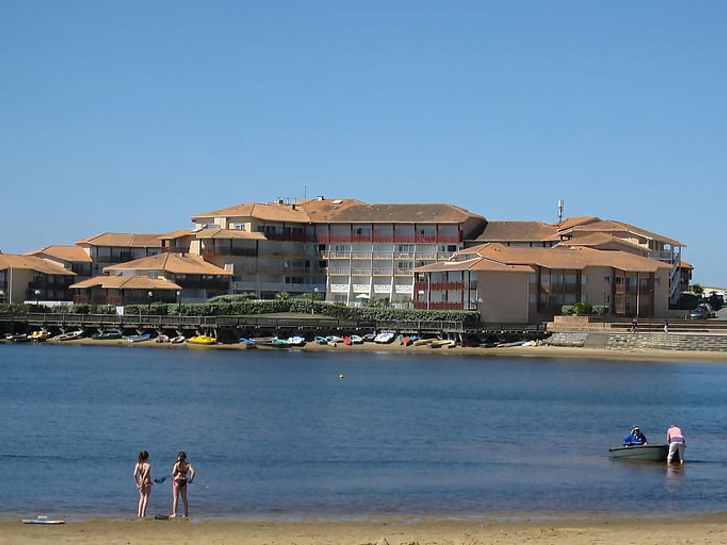 Un hotel costero con varias edificaciones, una playa y embarcaciones.