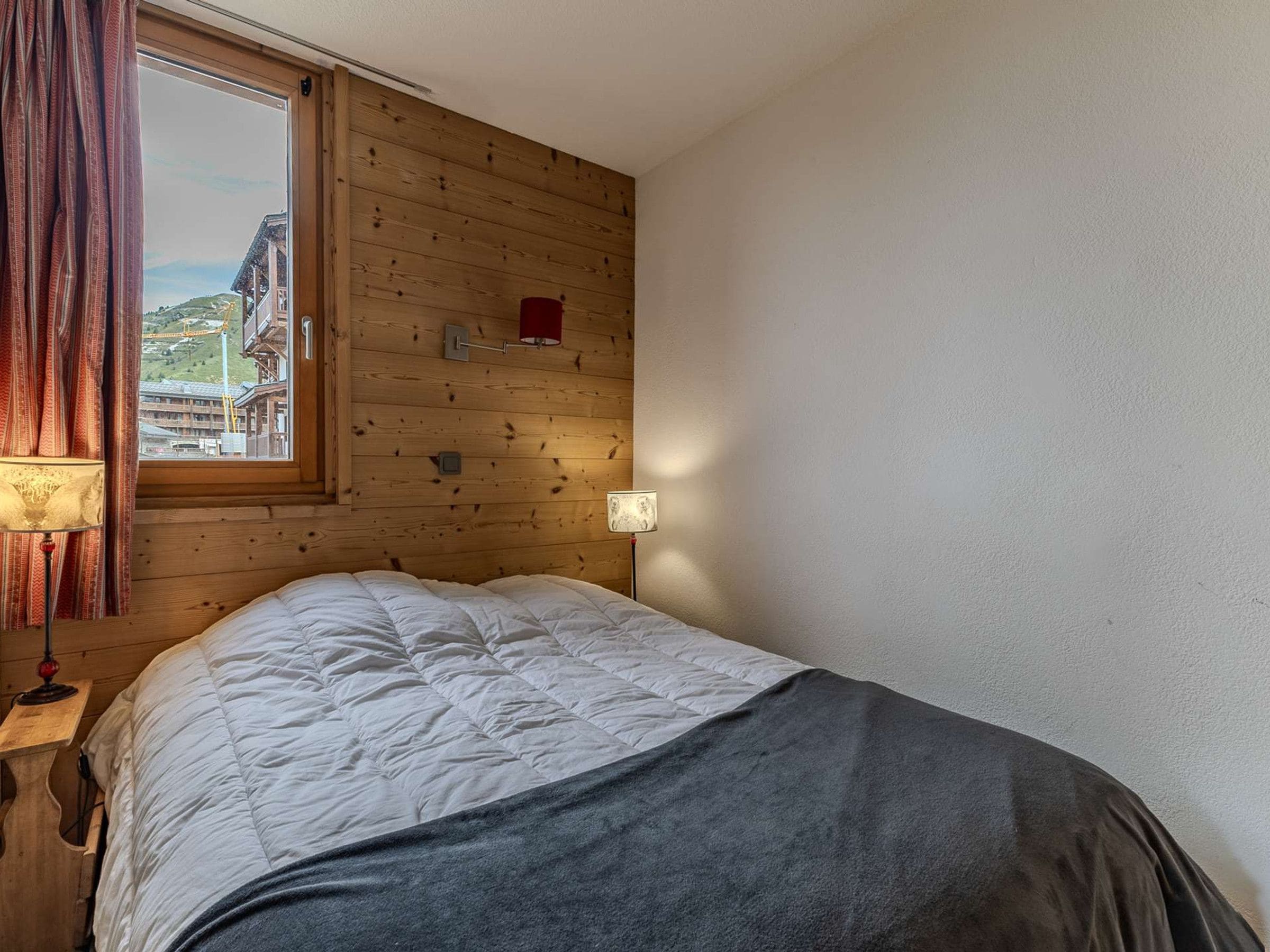 Una habitación con una cama, una ventana con cortinas, una lámpara y una luz empotrada en la pared.