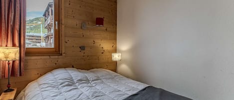 A room with a bed, a window with curtains, a lamp, and a wall-mounted light fixture.