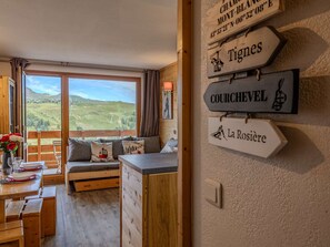 A cozy room with a wooden bench, a dining table, and a view of a green landscape. There are signs on the wall indicating 'Tignes', 'COURCHEVEL', and 'La Rosière'. - Apartment, panoramic view - 4 guests (Belle Plagne)