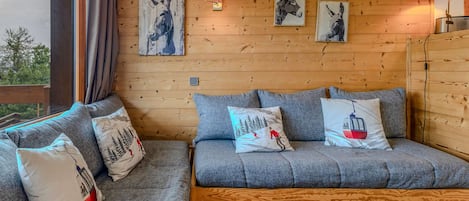 A cozy room with a sofa and cushions, wooden wall paneling, and artwork.