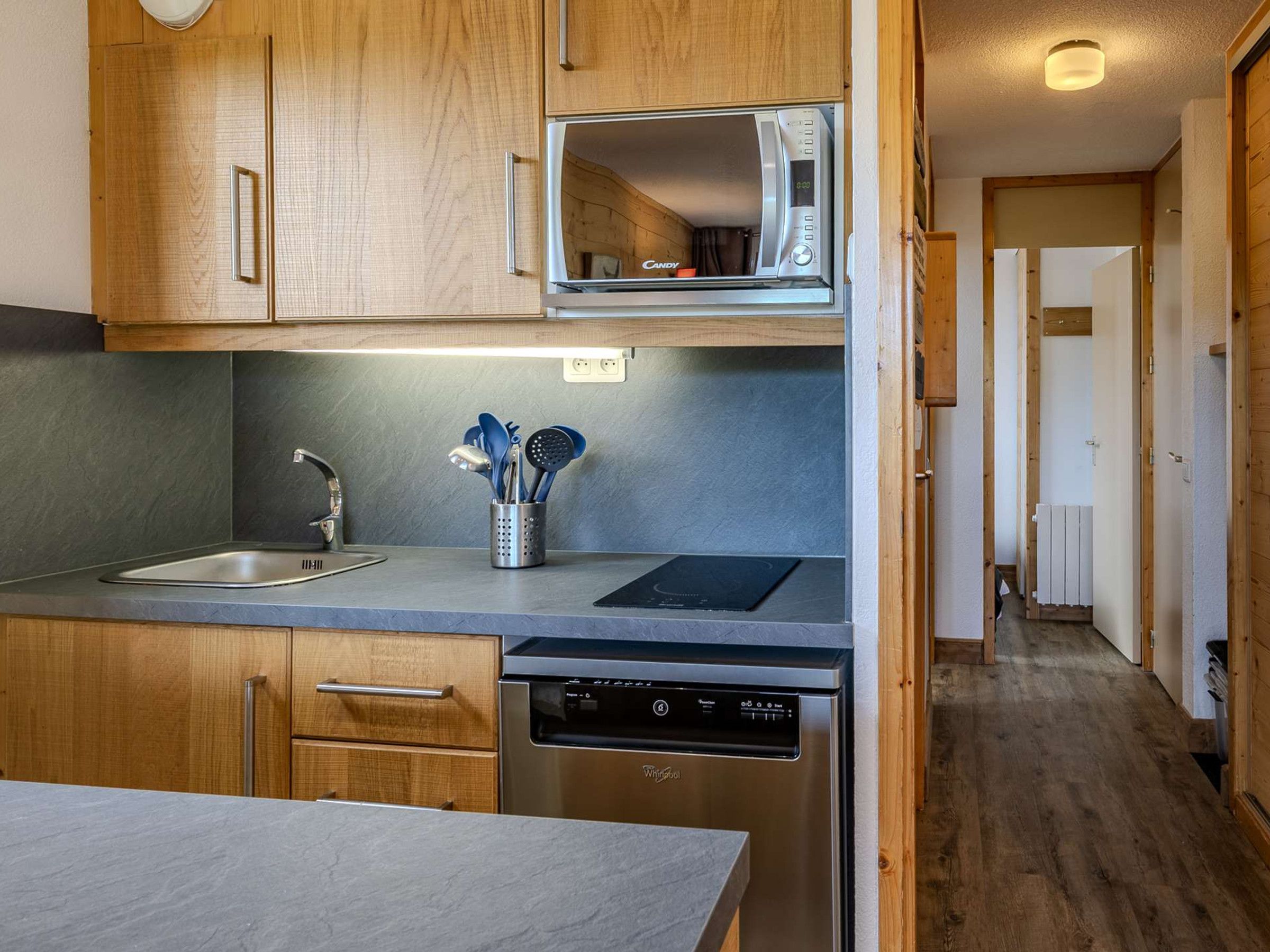 Una cocina compacta con armarios de madera, microondas, lavavajillas y una encimera con un portalapices.