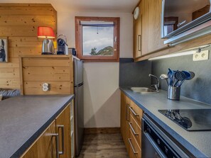 A compact kitchen with wooden cabinets, a built-in oven, a sink with a modern faucet, and a window providing natural light. - Apartment, panoramic view - 4 guests (Belle Plagne)