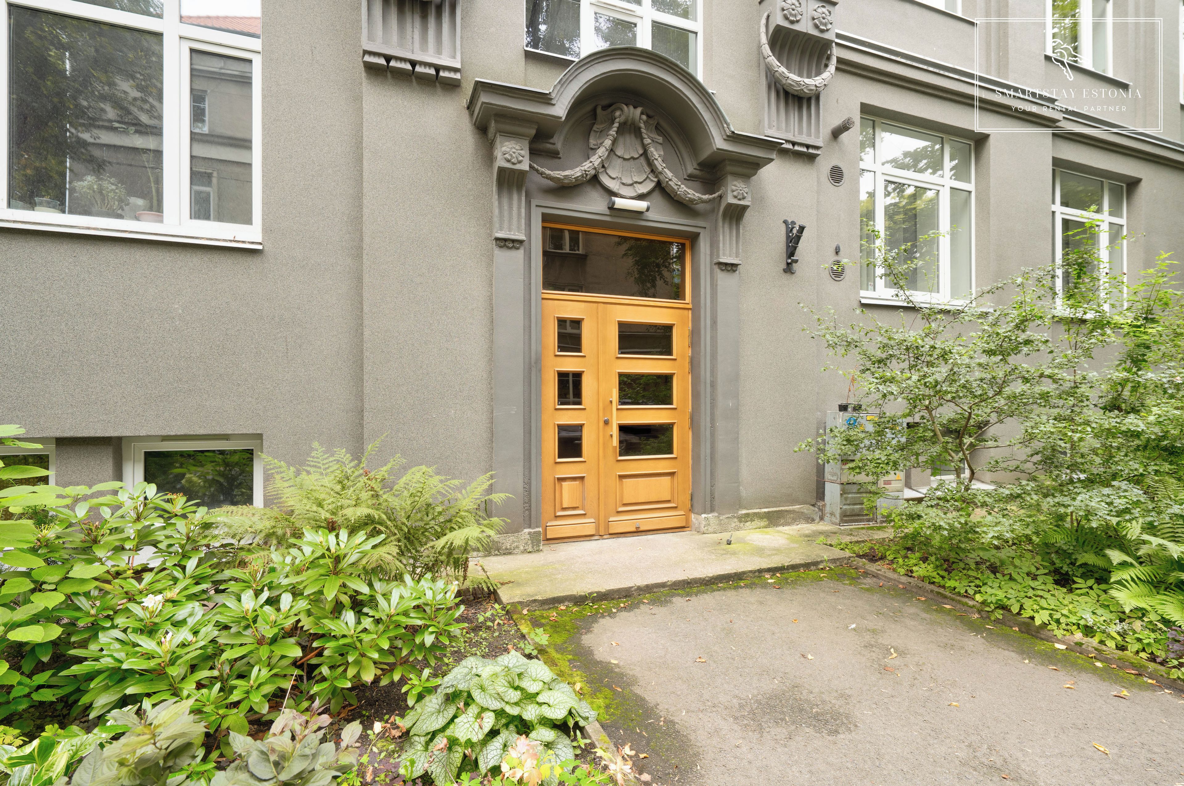 A building with a large wooden door, a small porch, and a garden with various plants.