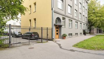 Ein zweistöckiges Gebäude mit gelbem Mauerwerk und einem grauen oberen Bereich. Vor dem befriedeten Parkplatz stehen Autos.