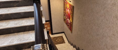 Una escalera con escalones de mármol y barandilla negra con detalles dorados.