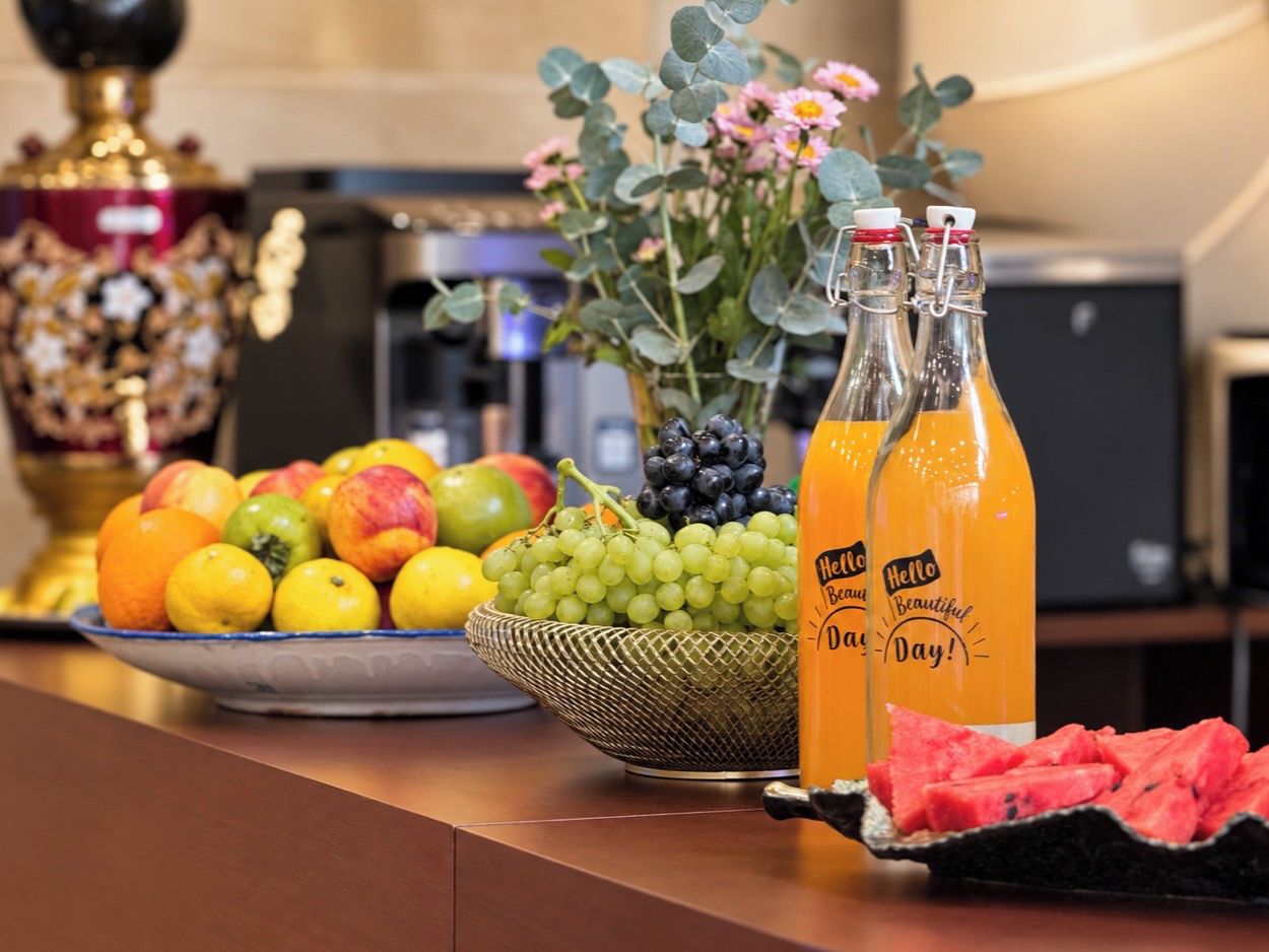 A fruit bowl with oranges, lemons, and grapes, two bottles of orange juice, and a vase with flowers on a kitchen counter.