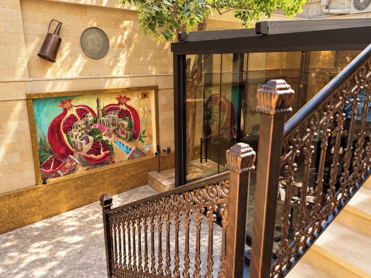 Una escalera con barandales metálicos ornamentados, un vidrio y un mural colorido en la pared.