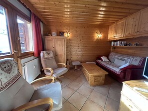 A cozy cabin interior with wooden walls, a sofa, a chair, a small table, and a cabinet. - 3-Room Apartment in Méribel - Sleeps 6 (Méribel)
