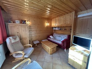 A cozy cabin interior with wooden walls, a sofa, a chair, a small table, and a television. - 3-Room Apartment in Méribel - Sleeps 6 (Méribel)